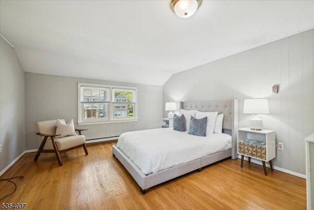 bedroom featuring baseboards, wood finished floors, lofted ceiling, and a baseboard radiator
