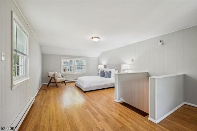 bedroom featuring baseboards, light wood-style flooring, a baseboard heating unit, and multiple windows