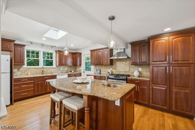 kitchen featuring white appliances, wall chimney range hood, light wood-type flooring, a sink, and a skylight