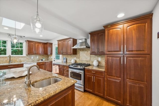 kitchen with gas stove, wall chimney range hood, a sink, and decorative light fixtures
