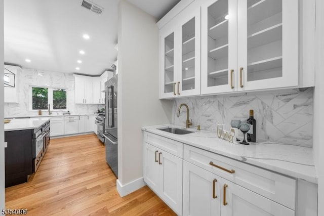 kitchen with a sink, white cabinets, tasteful backsplash, recessed lighting, and light stone countertops