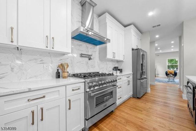 kitchen featuring high end appliances, wall chimney exhaust hood, white cabinets, tasteful backsplash, and recessed lighting