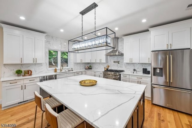 kitchen featuring appliances with stainless steel finishes, wall chimney range hood, a sink, light wood-style floors, and white cabinets