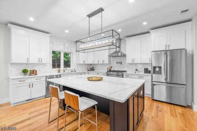kitchen featuring appliances with stainless steel finishes, wall chimney exhaust hood, white cabinets, light wood-style floors, and recessed lighting