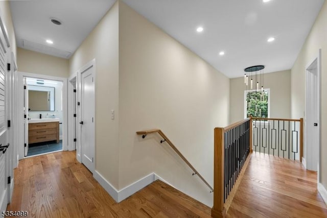 hall with an upstairs landing, light wood-style floors, baseboards, and recessed lighting