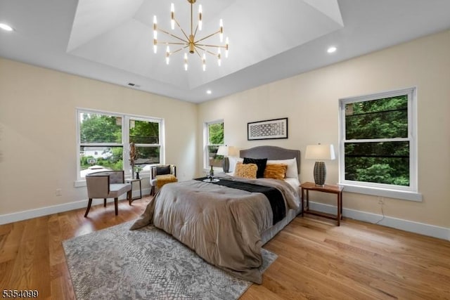 bedroom featuring baseboards, a tray ceiling, light wood finished floors, a chandelier, and recessed lighting