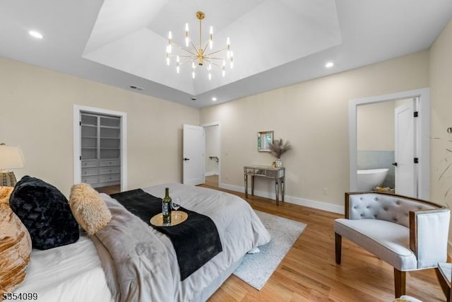 bedroom featuring a raised ceiling, light wood finished floors, a walk in closet, a chandelier, and recessed lighting