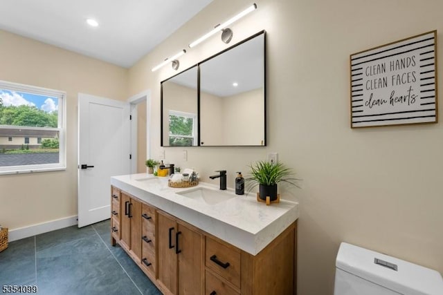 bathroom featuring toilet, double vanity, baseboards, tile patterned floors, and recessed lighting