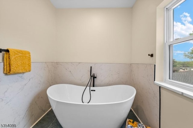 bathroom with a soaking tub, a wainscoted wall, and tile walls