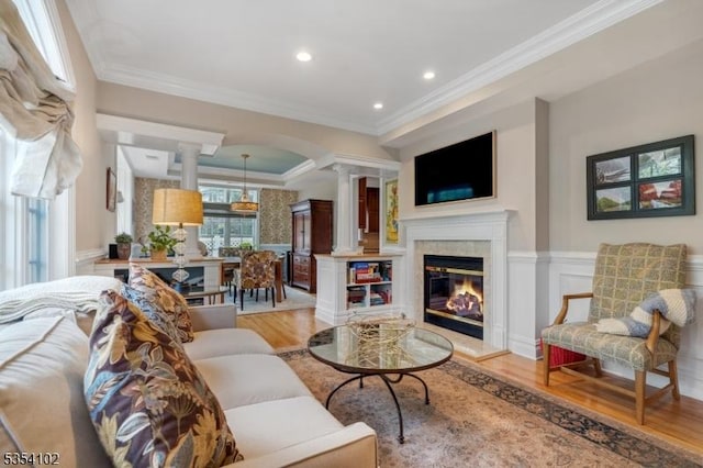 living room with light wood-style floors, a wainscoted wall, crown molding, and decorative columns