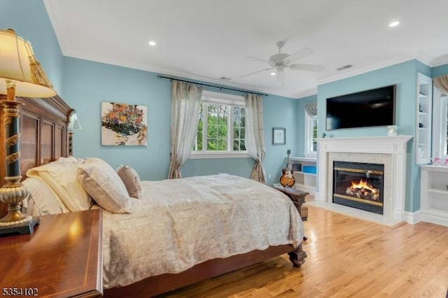 bedroom with crown molding, a glass covered fireplace, recessed lighting, wood finished floors, and visible vents