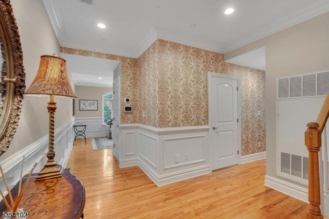 hallway featuring crown molding, light wood-style flooring, wainscoting, and wallpapered walls