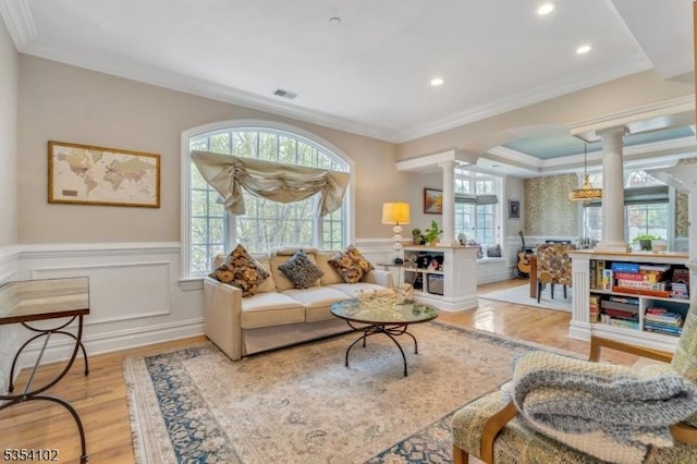 living area with ornate columns, visible vents, wainscoting, and light wood-type flooring