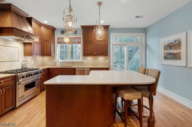 kitchen featuring a kitchen breakfast bar, stainless steel appliances, light wood finished floors, and custom range hood
