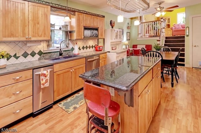 kitchen featuring stainless steel dishwasher, a kitchen island, light wood-style floors, tasteful backsplash, and a sink