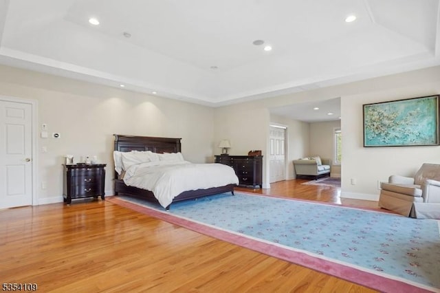 bedroom with recessed lighting, a tray ceiling, baseboards, and light wood-style floors