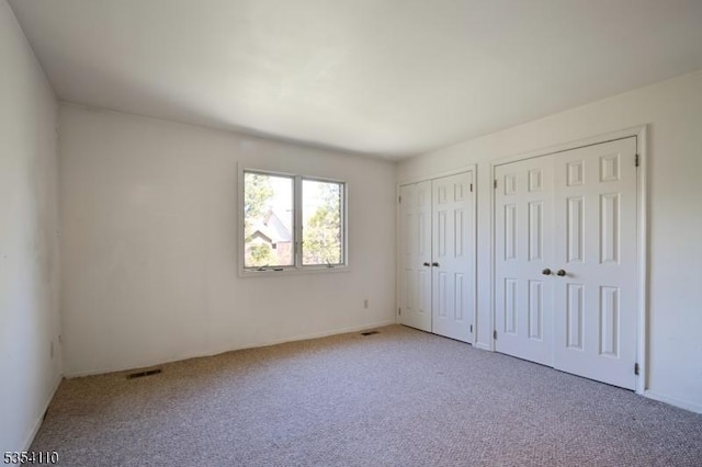 unfurnished bedroom featuring multiple closets, carpet floors, and visible vents