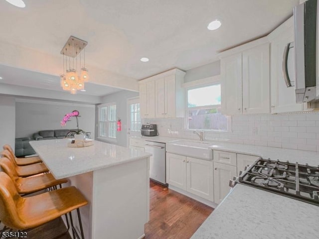 kitchen featuring stainless steel dishwasher, white cabinetry, a kitchen island, and a sink