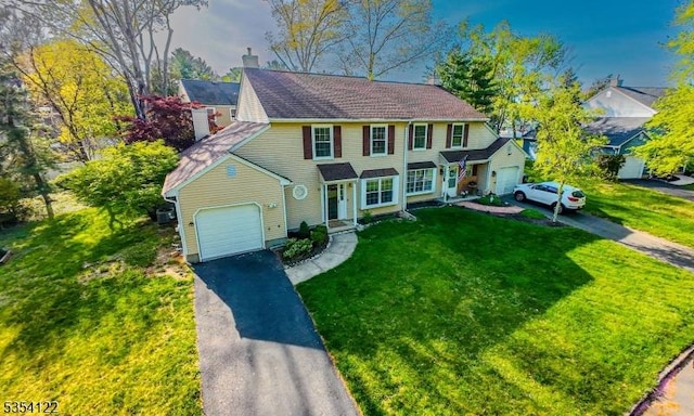 view of front of house featuring an attached garage, driveway, a chimney, and a front yard