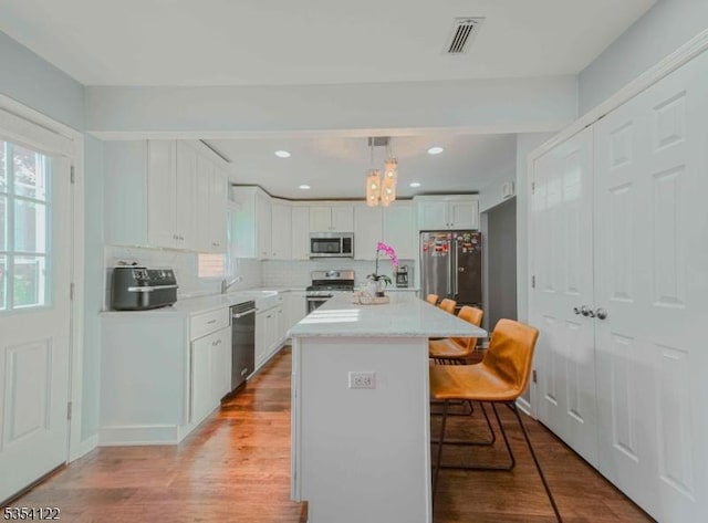 kitchen featuring decorative backsplash, appliances with stainless steel finishes, light wood-type flooring, white cabinets, and a breakfast bar