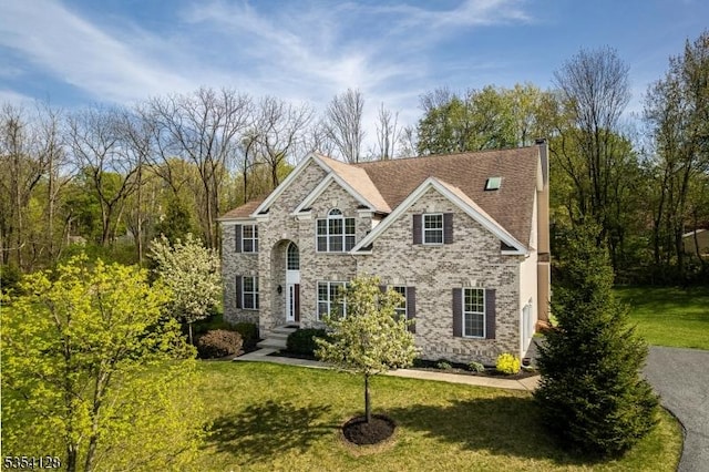 traditional-style house featuring a chimney, stone siding, and a front yard