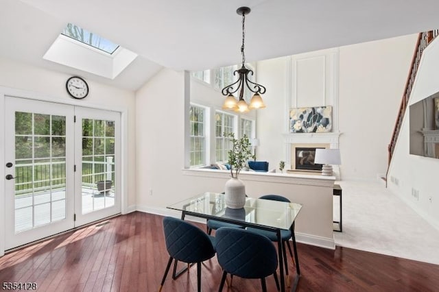 dining area with a skylight, a notable chandelier, a glass covered fireplace, and dark wood finished floors