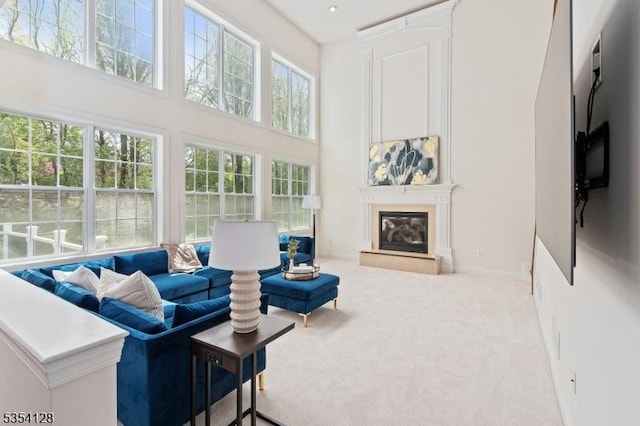 living area featuring carpet floors, a glass covered fireplace, a towering ceiling, and baseboards