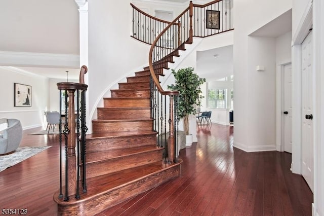 staircase with baseboards, hardwood / wood-style flooring, and a towering ceiling