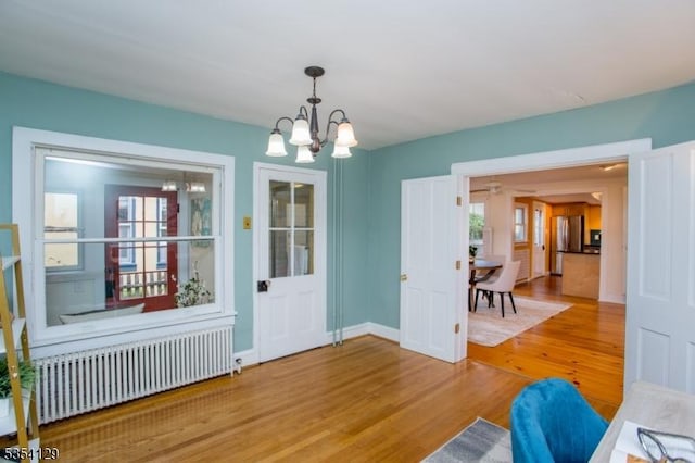 interior space with radiator heating unit, a wealth of natural light, wood finished floors, and a notable chandelier