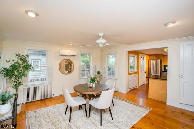 dining room featuring crown molding, radiator heating unit, an AC wall unit, a ceiling fan, and light wood-style flooring