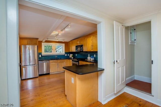 kitchen featuring dark countertops, a sink, light wood-style floors, stainless steel appliances, and a peninsula
