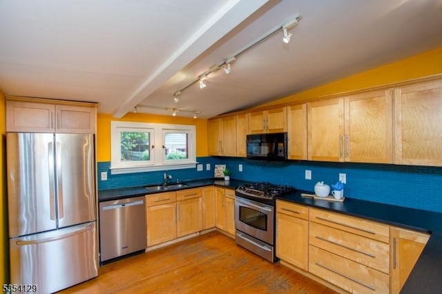 kitchen with dark countertops, appliances with stainless steel finishes, track lighting, a sink, and tasteful backsplash
