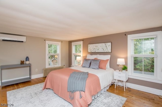 bedroom with an AC wall unit, baseboards, radiator heating unit, and wood finished floors
