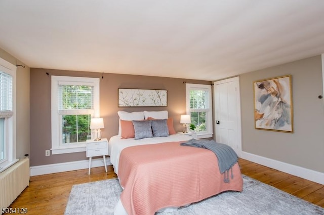 bedroom with radiator heating unit, baseboards, and wood finished floors