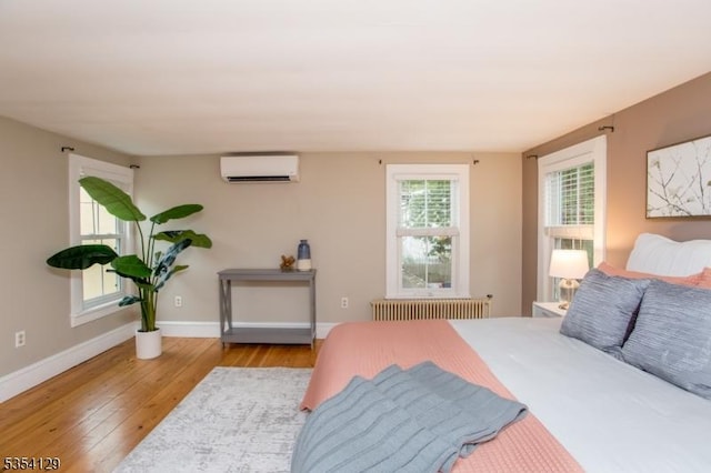 bedroom featuring an AC wall unit, baseboards, radiator heating unit, and hardwood / wood-style flooring