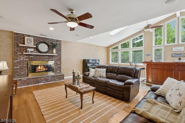 living area with light wood finished floors, a fireplace, a ceiling fan, recessed lighting, and a skylight