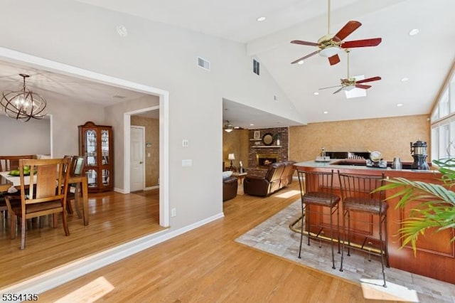 interior space featuring a brick fireplace, light wood-style flooring, ceiling fan with notable chandelier, and beam ceiling