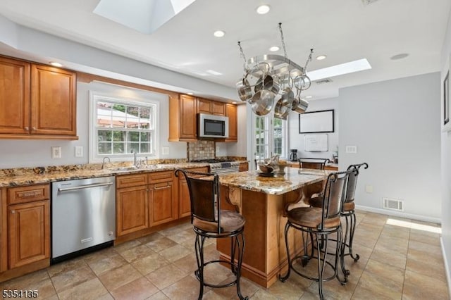 kitchen featuring visible vents, a center island, a sink, appliances with stainless steel finishes, and a skylight