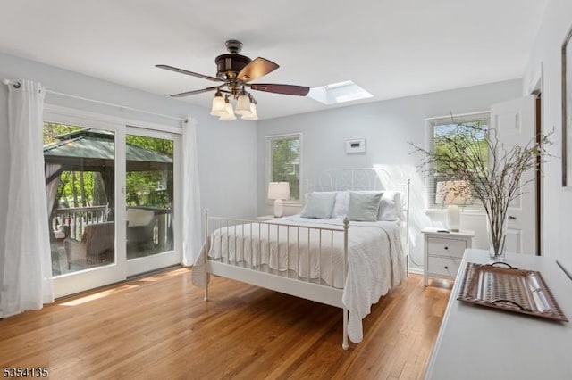 bedroom with access to outside, a skylight, multiple windows, and wood finished floors