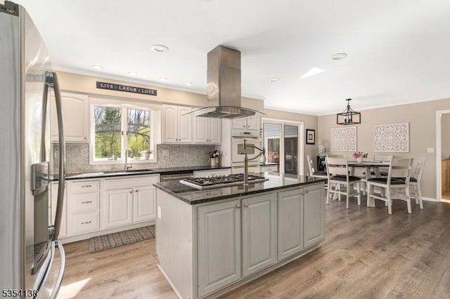 kitchen with a sink, appliances with stainless steel finishes, ornamental molding, and island exhaust hood