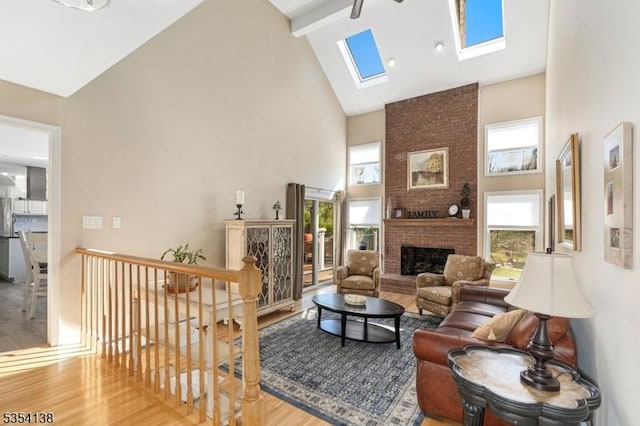 living area with beam ceiling, a fireplace, high vaulted ceiling, wood finished floors, and a skylight
