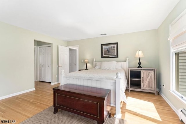 bedroom featuring light wood-type flooring, baseboards, baseboard heating, and visible vents