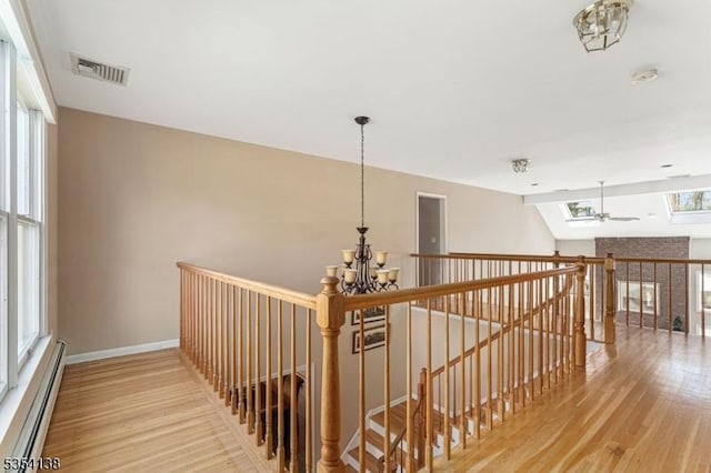 corridor featuring visible vents, an inviting chandelier, wood finished floors, baseboard heating, and an upstairs landing