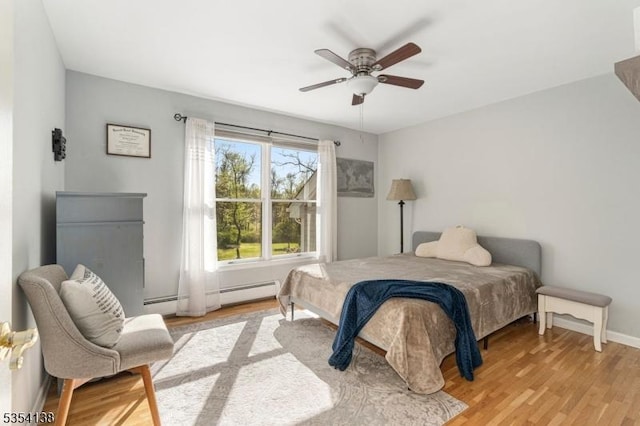 bedroom with baseboards, baseboard heating, a baseboard heating unit, a ceiling fan, and light wood-style flooring