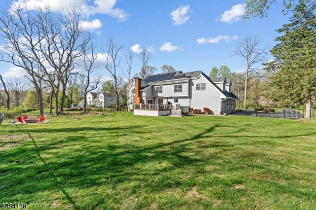 back of property featuring a lawn, a chimney, fence, and a wooden deck