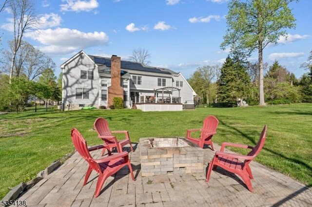 exterior space with roof mounted solar panels, a chimney, a lawn, a patio, and a fire pit