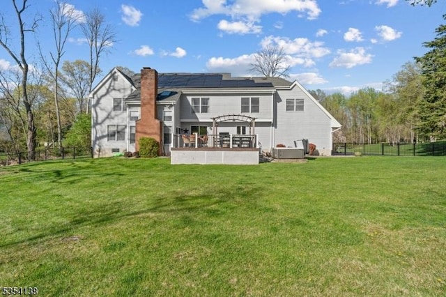 back of house featuring a pergola, roof mounted solar panels, a fenced backyard, a chimney, and a yard