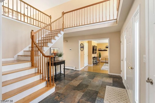 foyer featuring stone finish floor, a towering ceiling, stairway, baseboards, and a baseboard heating unit
