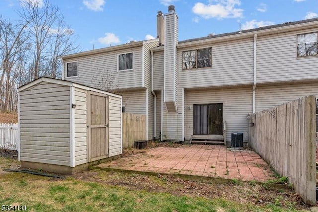 back of house featuring an outdoor structure, fence, a shed, a chimney, and a patio area