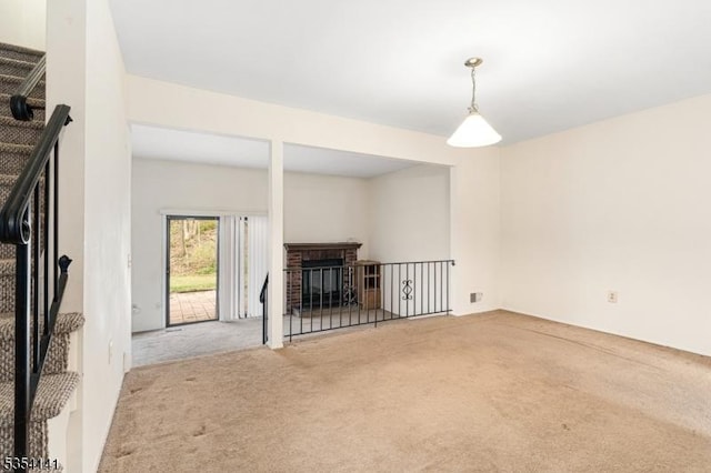 unfurnished living room with carpet floors, stairs, and a brick fireplace